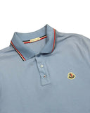 DRIPNORD light blue cotton Moncler polo shirt with red, white, and black striped collar and Moncler logo patch.