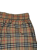 DRIPNORD Burberry Monogram Swim Shorts in beige, black, red, and white plaid pattern. Elastic waistband and pocket detail.